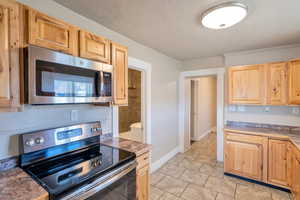 Kitchen featuring light brown cabinetry, a textured ceiling, stainless steel appliances, and baseboards