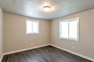 Empty room with dark wood-type flooring, plenty of natural light, baseboards, and visible vents