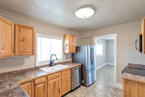 Kitchen with a sink, dark countertops, a textured ceiling, and appliances with stainless steel finishes