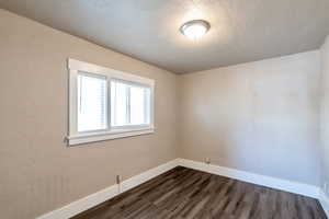 Spare room featuring a textured ceiling, dark wood-type flooring, baseboards, and a textured wall