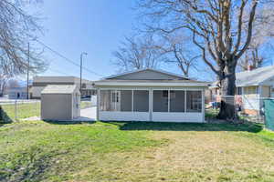 Back of property featuring an outdoor structure, a storage unit, a yard, and a sunroom