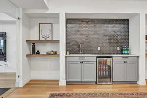 Bar with beverage cooler, baseboards, a sink, light wood-style floors, and backsplash