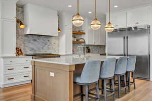 Kitchen featuring stainless steel built in fridge, light wood-style flooring, light countertops, and wall chimney range hood
