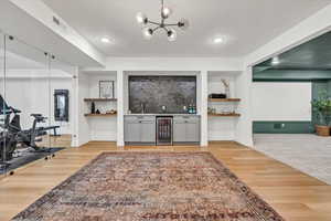 Bar featuring beverage cooler, visible vents, light wood-style flooring, a sink, and bar