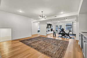 Workout area featuring visible vents, baseboards, light wood-style floors, a textured ceiling, and a chandelier