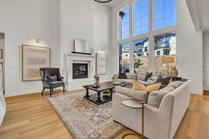 Living area featuring a glass covered fireplace, a high ceiling, light wood-style flooring, and baseboards