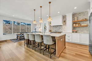 Kitchen with light countertops, light wood finished floors, a kitchen island with sink, and backsplash