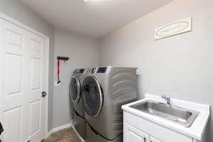 Clothes washing area with tile patterned flooring, a sink, washer and dryer, and cabinet space.