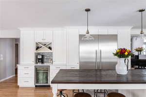 Kitchen featuring built in fridge, pendant lighting, light wood-style flooring, white cabinets, and beverage cooler