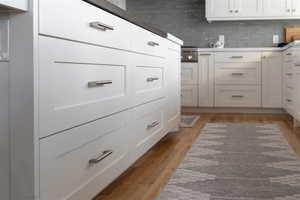 Details with light countertops, light wood finished floors, decorative backsplash, and white cabinets.