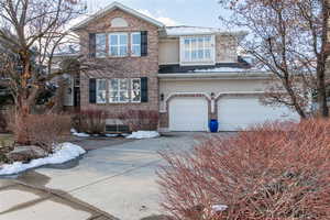 Traditional home featuring a 3 car garage, brick siding, driveway, and stucco siding.