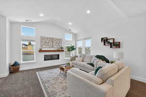 Living area featuring dark colored carpet, healthy amount of natural light, a glass covered fireplace, vaulted ceiling, and recessed lighting