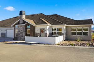 Ranch-style home featuring a fenced front yard, stucco siding, a garage, stone siding, and a chimney