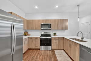 Kitchen featuring appliances with stainless steel finishes, hanging light fixtures, light wood-style floors, light stone counters, and modern cabinets
