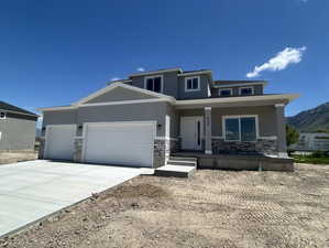 Prairie-style home featuring stucco siding, an attached garage, driveway, and stone siding