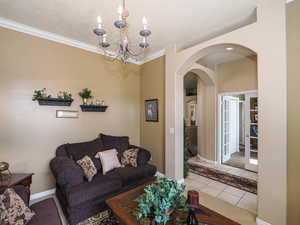 Tiled living area featuring a notable chandelier, ornamental molding, a textured ceiling, arched walkways, and baseboards