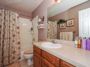 Bathroom with vanity, shower / bath combo, a textured ceiling, tile patterned floors, and toilet