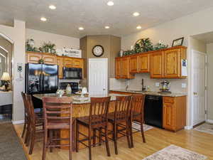 Kitchen with black appliances, a sink, a kitchen island, brown cabinetry, and light wood finished floors