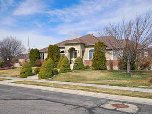 View of front of home featuring stucco siding, brick siding, roof with shingles, and a front lawn