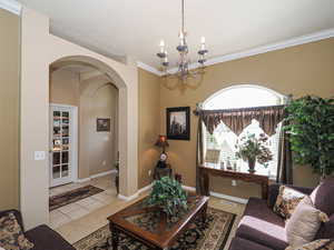 Tiled living room with visible vents, baseboards, arched walkways, crown molding, and a notable chandelier