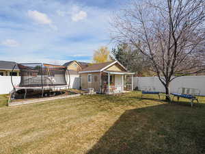 Back of house with an outdoor structure, a trampoline, a fenced backyard, and a lawn