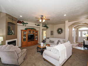 Living room with light colored carpet, arched walkways, a textured ceiling, and a glass covered fireplace