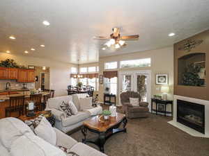 Living room featuring ceiling fan, carpet, a fireplace with flush hearth, recessed lighting, and a textured ceiling