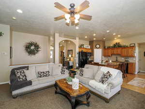 Living room with a textured ceiling, recessed lighting, arched walkways, light wood finished floors, and baseboards