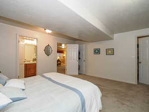 Bedroom with light colored carpet, a textured ceiling, ensuite bathroom, and baseboards