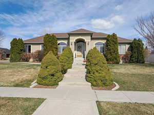 View of front of house with stucco siding, a front yard, and a shingled roof