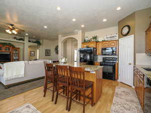 Kitchen with arched walkways, black appliances, a center island, and light wood finished floors