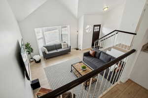 Living room with light wood finished floors, high vaulted ceiling, baseboards, and stairs