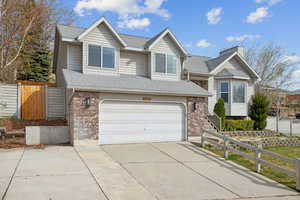 View of front of house with roof with shingles, fence, brick siding, an attached garage, and driveway