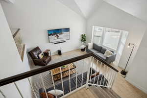 Living area featuring light wood-style flooring, high vaulted ceiling, and baseboards