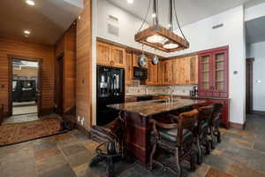 Kitchen with a center island with sink, dark stone counters, a kitchen breakfast bar, stone tile flooring, and recessed lighting