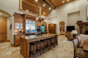 Kitchen with arched walkways, brown cabinets, high vaulted ceiling, a wooden ceiling with exposed beams, and dark stone counters