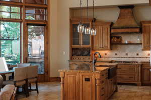Kitchen featuring custom range hood, stone tile flooring, light stone counters, stainless steel gas stovetop, and decorative backsplash