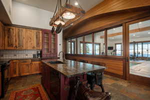 Kitchen with a center island with sink, glass insert cabinets, black appliances, a kitchen breakfast bar, and stone tile flooring