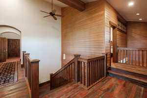 Stairs with wooden walls, wood-type flooring, recessed lighting, ceiling fan, and beam ceiling