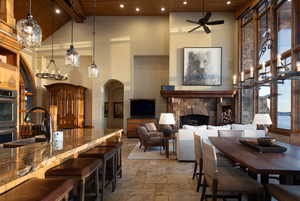 Dining room with a chandelier, a stone fireplace, high vaulted ceiling, recessed lighting, and stone tile floors