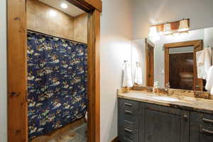 Bathroom featuring vanity, curtained shower, and stone finish floors