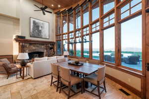 Dining space featuring a stone fireplace, a high ceiling, a ceiling fan, wood ceiling, and recessed lighting