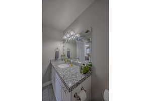 Half bath with baseboards, lofted ceiling, toilet, and vanity
