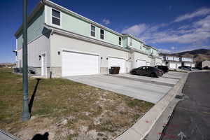 View of side of home featuring driveway, a yard, an attached garage, stucco siding, and a residential view