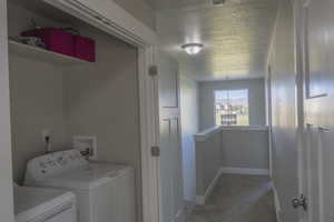 Laundry room with light carpet, washer and dryer, a textured ceiling, baseboards, and laundry area