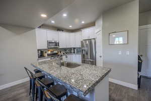 Kitchen with backsplash, dark wood finished floors, a kitchen bar, stainless steel appliances, and a sink