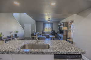 Kitchen with a sink, dark stone countertops, stainless steel dishwasher, open floor plan, and ceiling fan