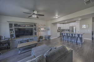Living area with dark wood-style floors, visible vents, a ceiling fan, and baseboards