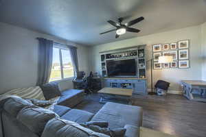 Living room featuring dark wood finished floors, a ceiling fan, baseboards, and a textured ceiling
