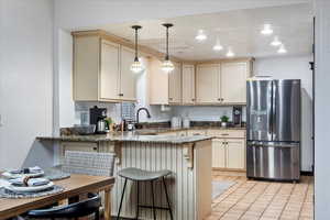 Kitchen with stainless steel fridge with ice dispenser, dark stone countertops, a peninsula, hanging light fixtures, and a sink